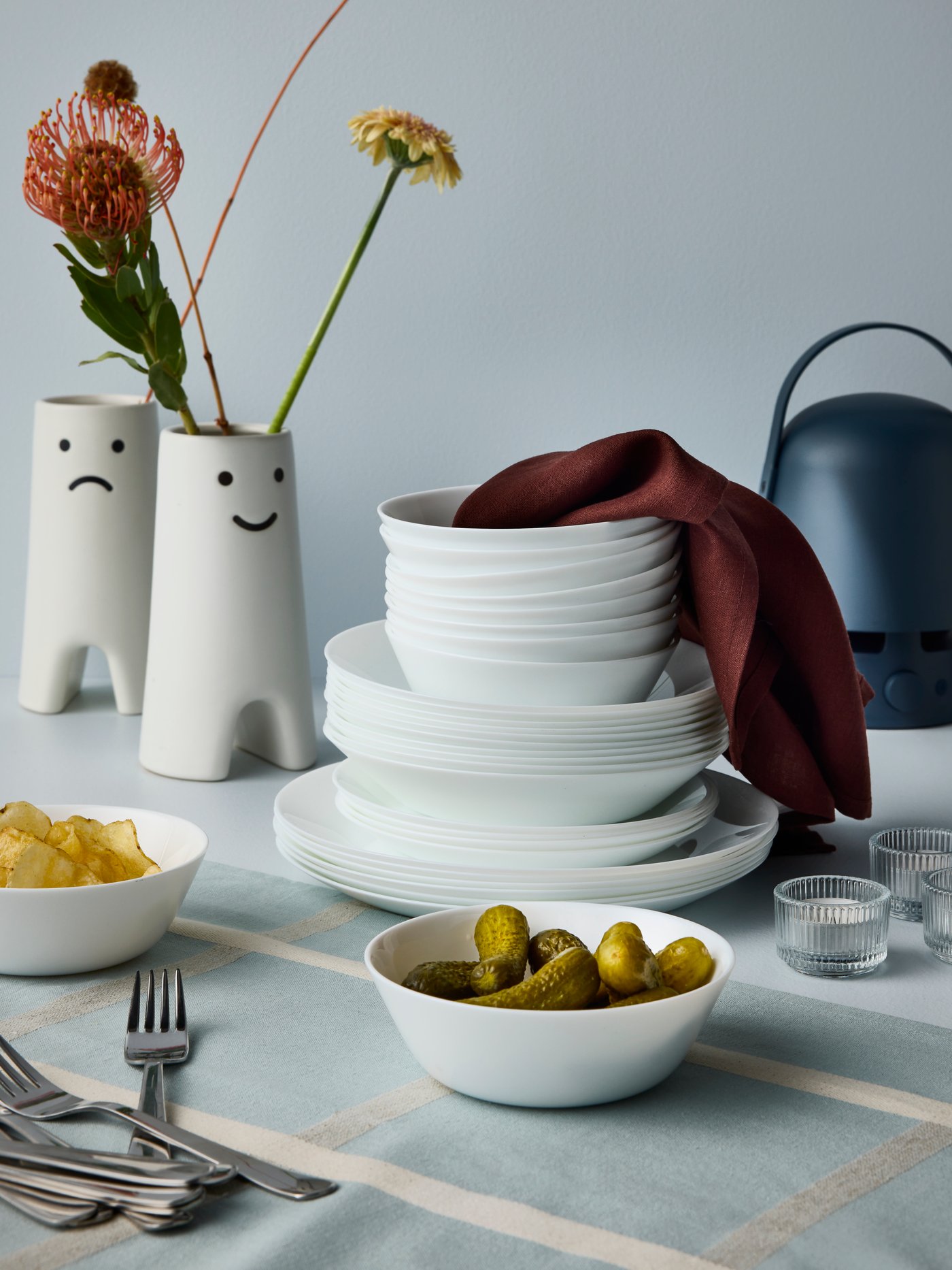 White bowls and plates from the OFTAST series are placed on a table, some of them stacked, and there are two FRÖVÄXT vases.