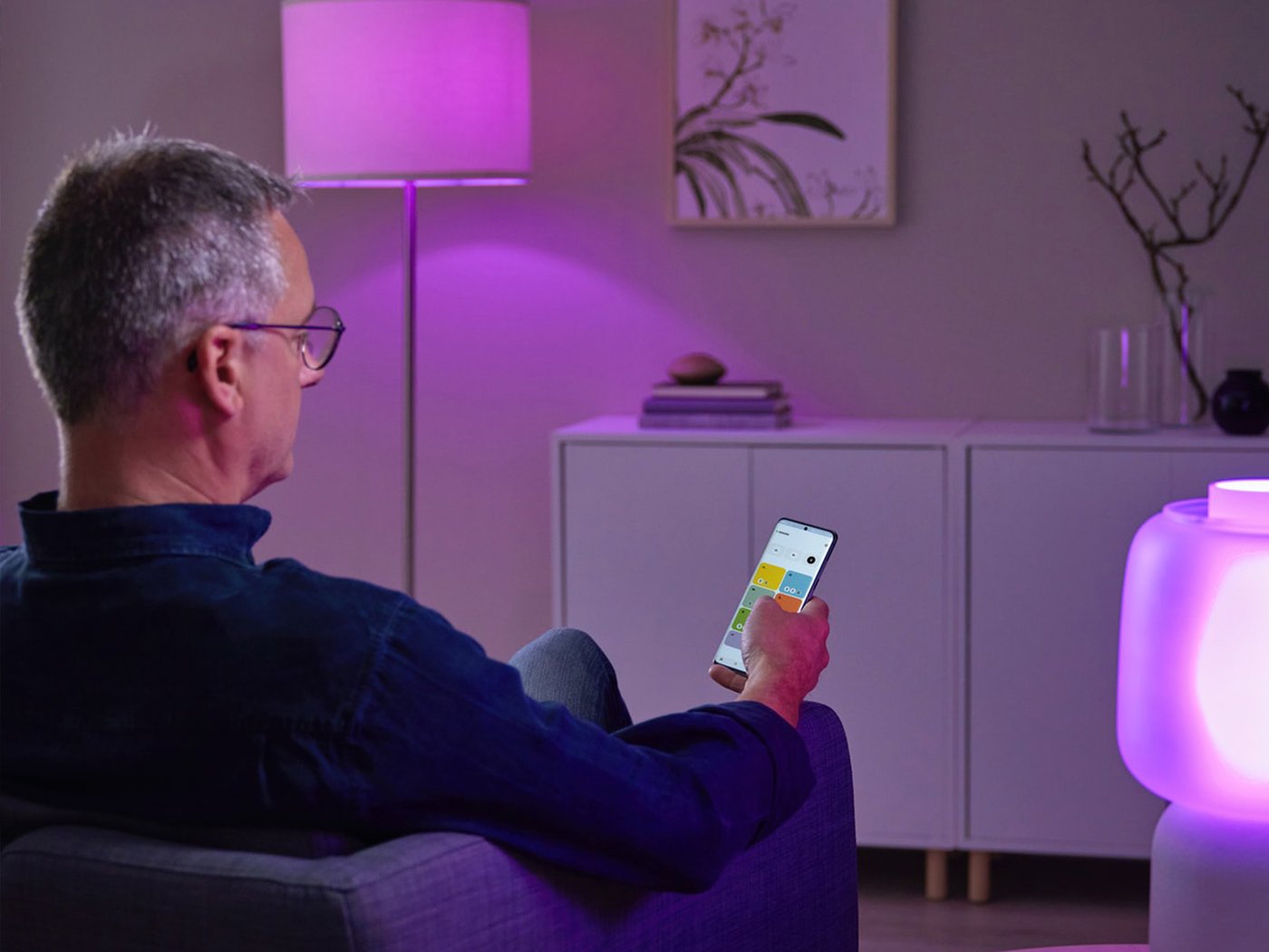 Čovek sedi u fotelji, drži mobilni uređaj i gleda aplikaciju IKEA Home smart koju omogućava DIRIGERA baza.