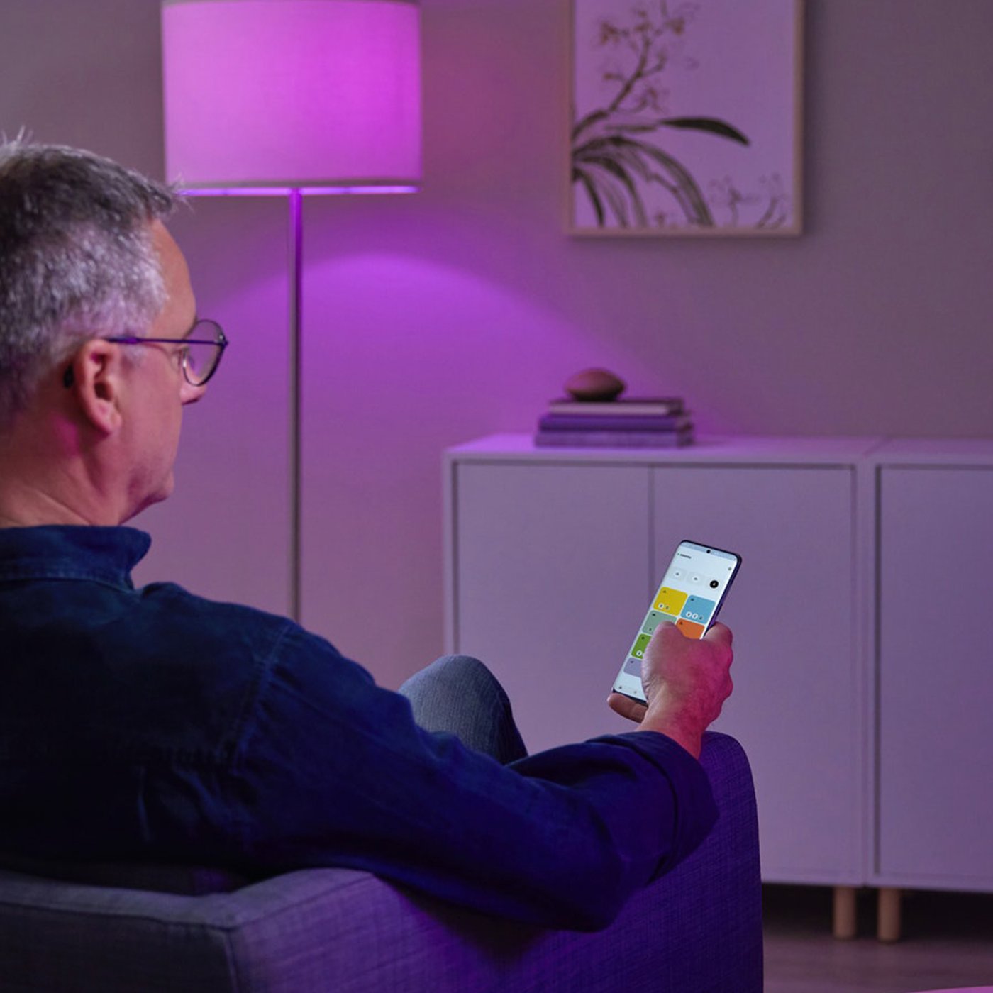 En mand sidder i en stol med en mobilenhed i hånden og ser på IKEA Home smart app aktiveret af DIRIGERA hub.