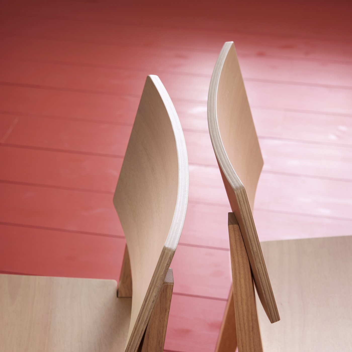 Two KARSKÄR chairs are standing on a red floor, back to back, highlighting the rubberwood material. 