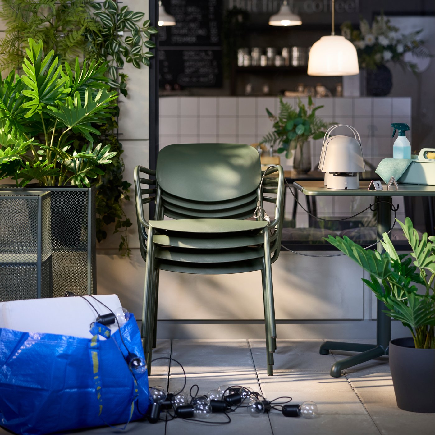 Outdoor café scene featuring four stacked deep green VISINGSÖ chairs next to plants and warm ambient lighting.