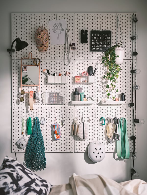 Six SKÅDIS pegboards together on a wall with various containers on it holding things like make up, accessories and a plant.