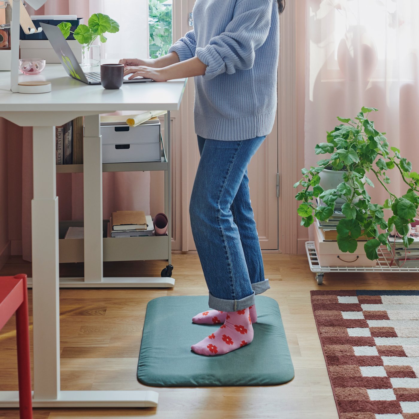 Person som står vit ett skrivbord på en ståmatta. 