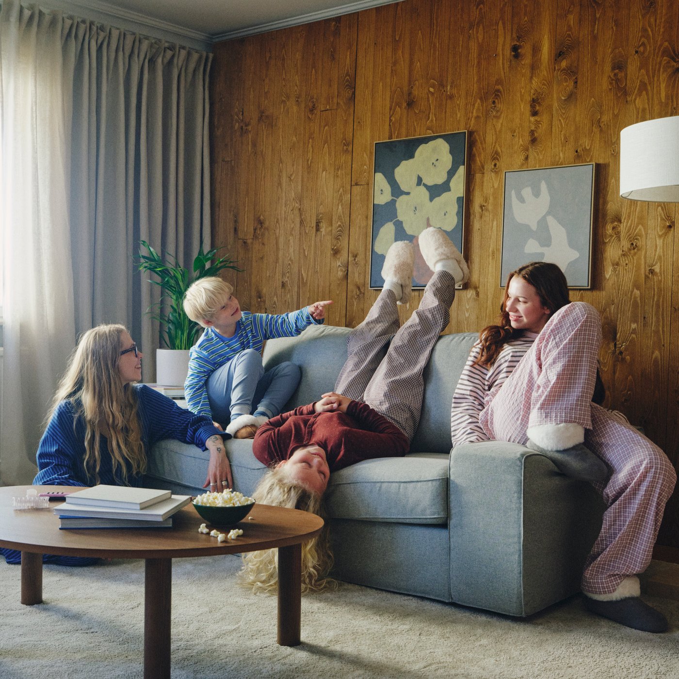 A KIVIK two-seat Tibbleby beige/grey sofa is against a wood-paneled wall. An adult and three children lounge on the sofa.