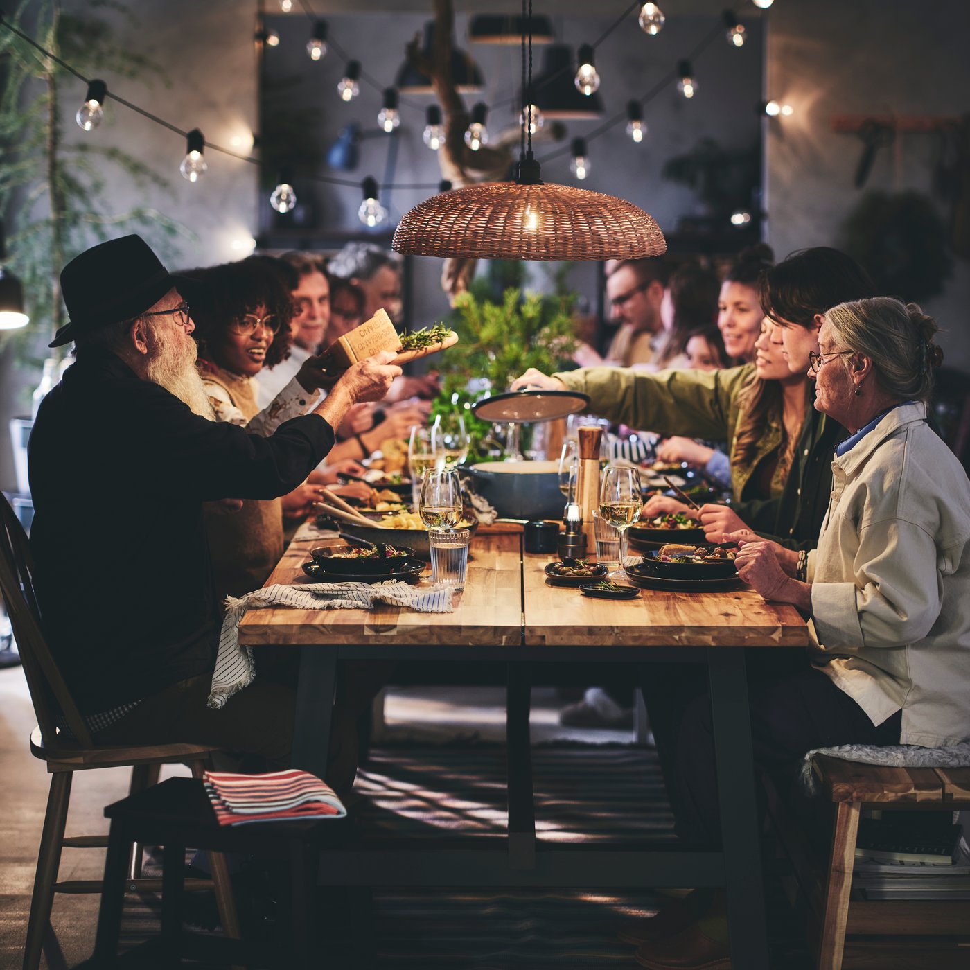 An elderly couple seated at the end of a long table surrounded by seated dinner guests of all ages.
