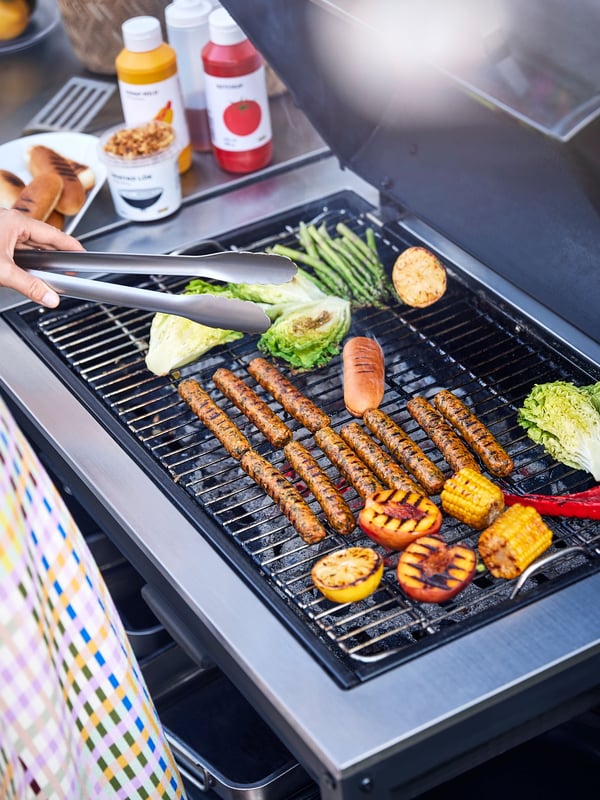 Iemand bakt enkele KORVMOJ veggiehotdogs en groente op de barbecue.