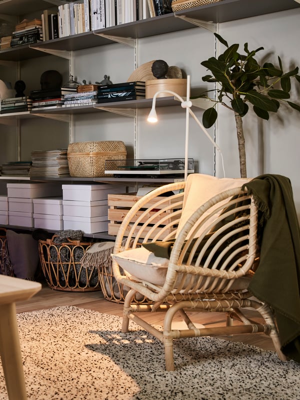 Soggiorno con un tavolino in impiallacciatura di frassino, una poltrona in rattan, un tappeto con pelo lungo e mensole con libri.