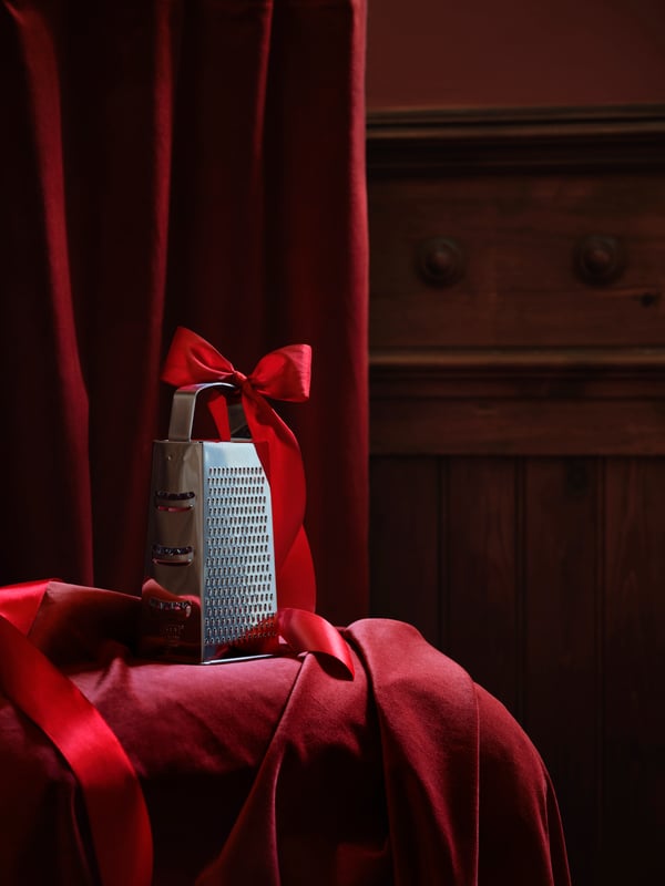 Close-up of kitchen corner with red curtains, stainless steel grater with a red ribbon on the handle, red household textile.