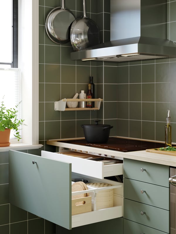 Armoire de cuisine avec façade NICKEBO gris-vert dont un tiroir est ouvert, laissant entrevoir des ustensiles de cuisine.