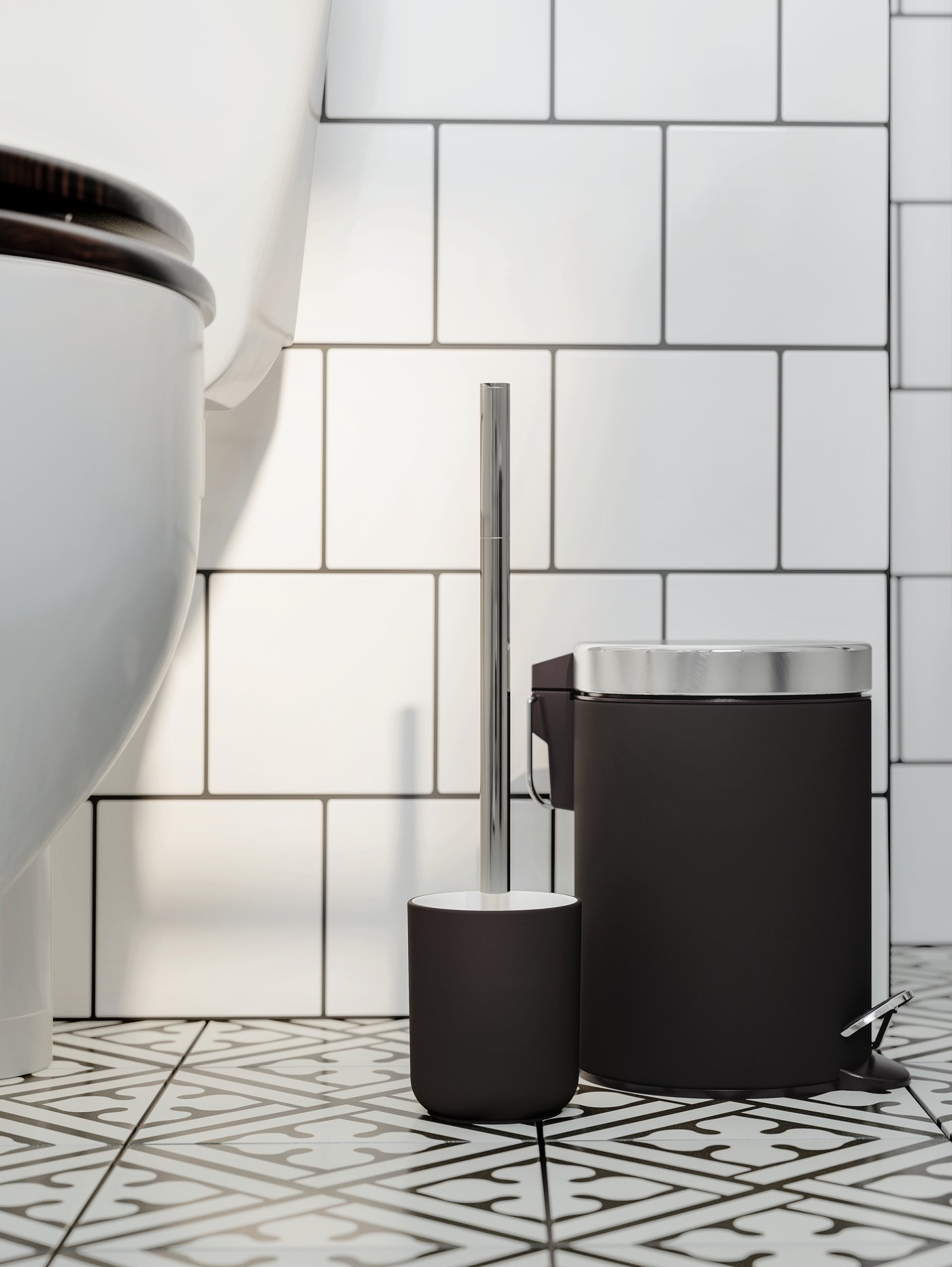 EKOLN waste bin and EKOLN toilet brush in dark grey/stainless steel stand on a black/white tiled floor next to a toilet.