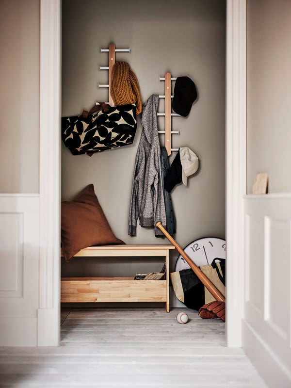 A hallway with a pine PERJOHAN bench with storage below two PLOGA vertical hook racks with items hanging from them.