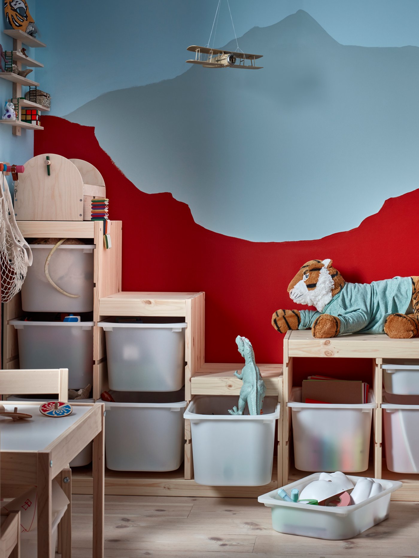 A children’s room with a mountain scene painted on the wall with toys and lots of TROFAST storage in front of it.