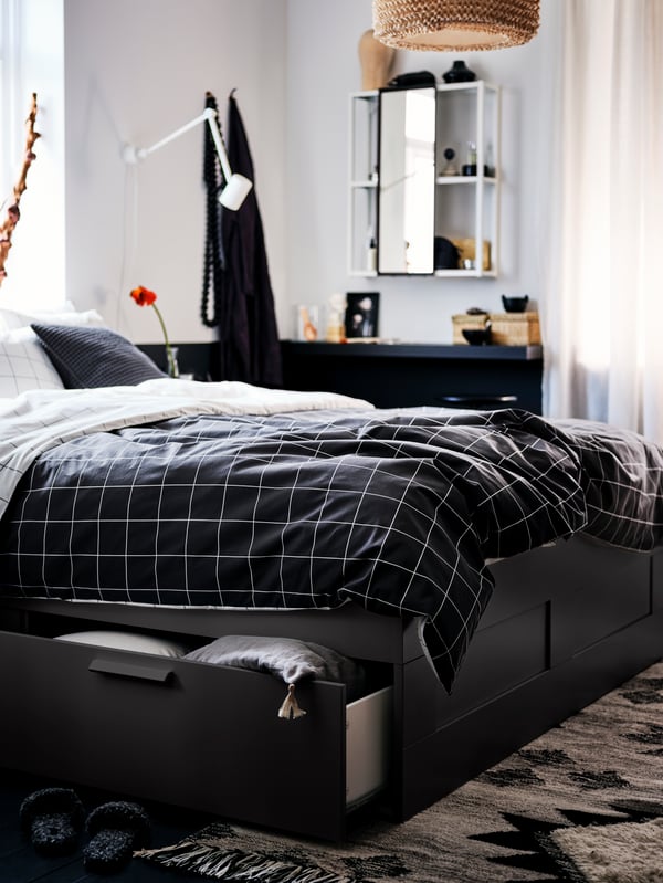 Une chambre à coucher avec un lit BRIMNES noir avec rangement, fait avec du linge de lit carrelé VITKLÖVER, et une armoire à pharmacie ENHET.