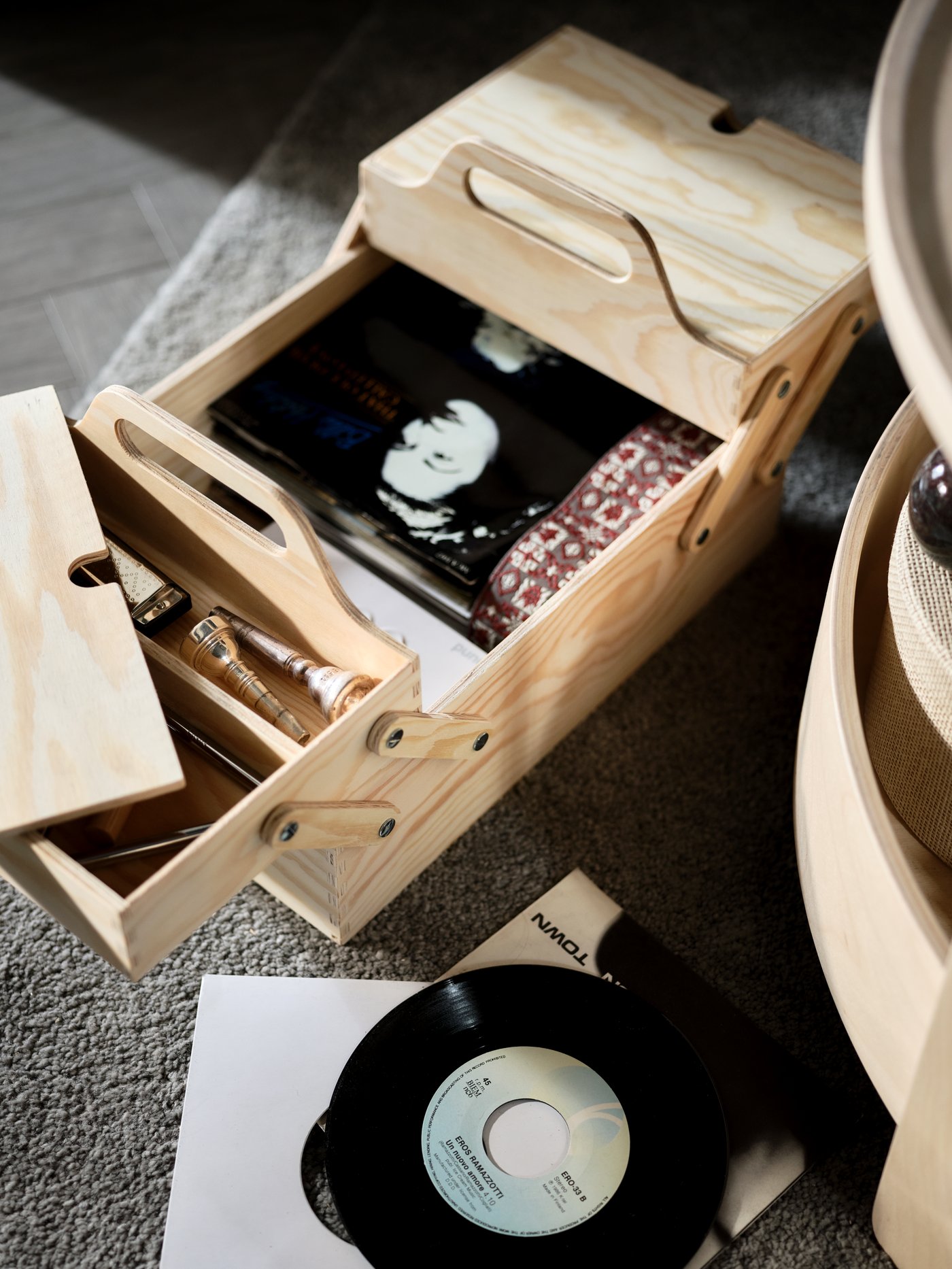 A KLÄMMEMACKA desk organiser in natural plywood is open and there are different personal items inside. Next to the organiser there is a small vinyl record.