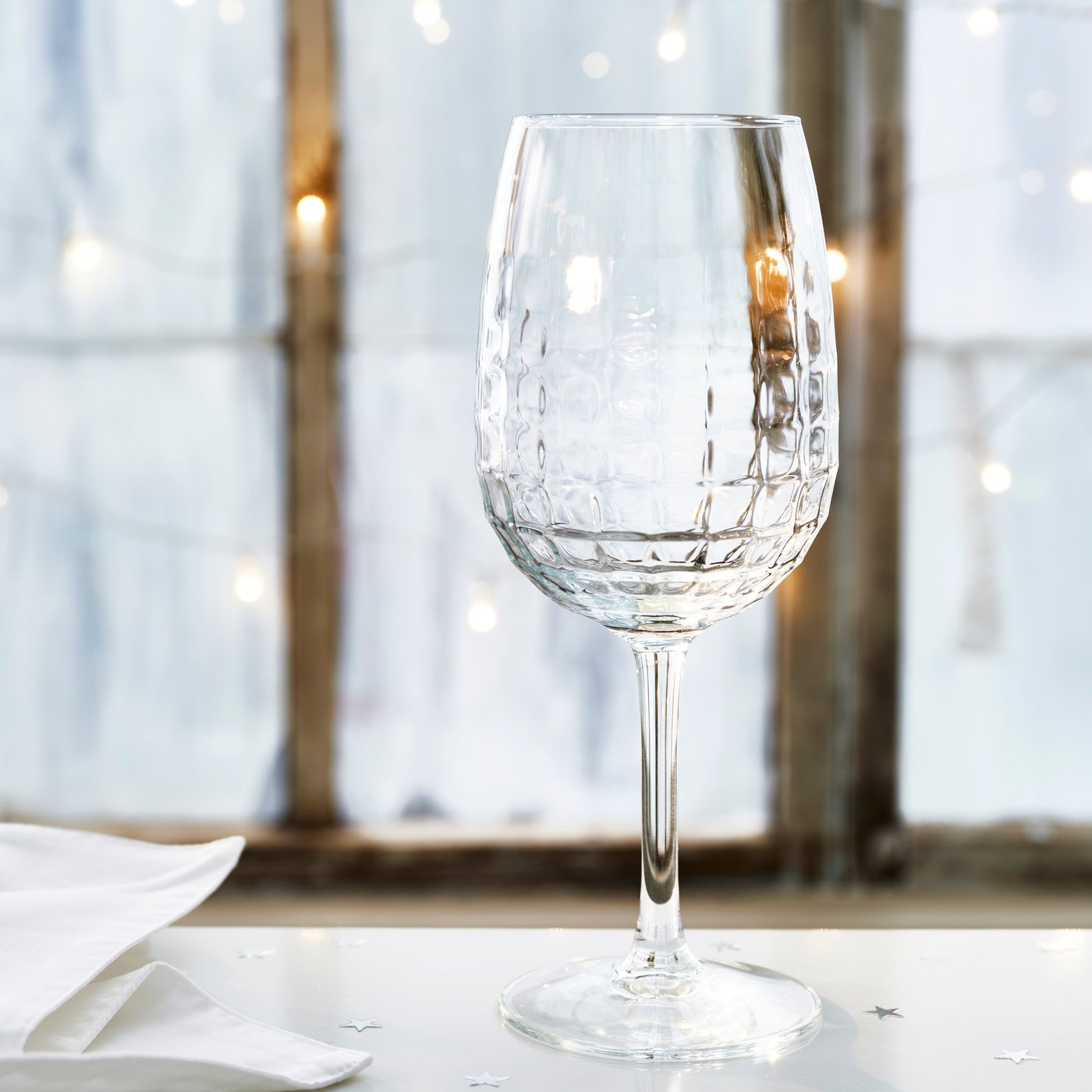 Elegant vinglas i klart glas med dekorativ struktur, placerat på dukat bord.