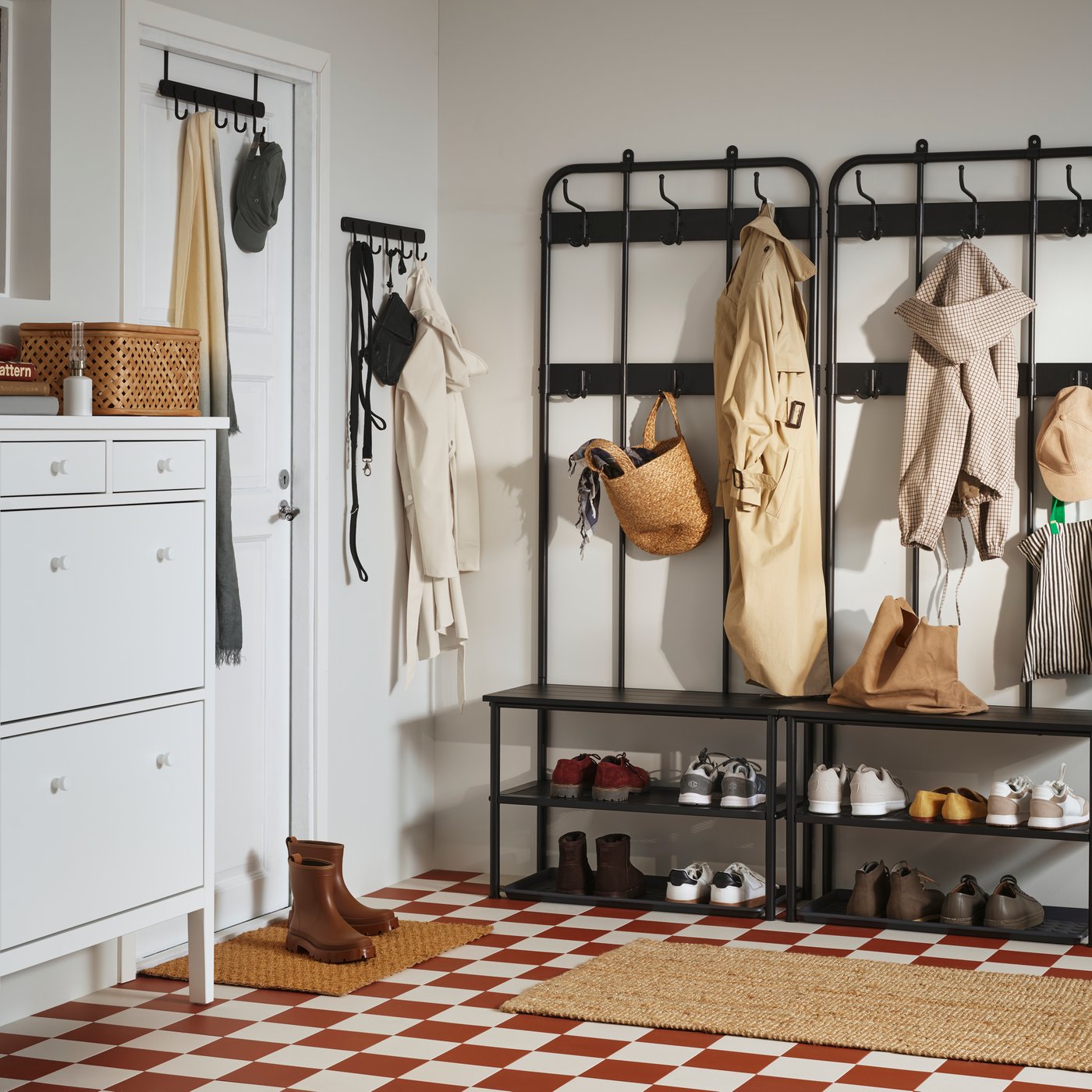 A hallway with a checked floor featuring a black NIPÅSEN coat rack with coats and shoes on and a white GULLABERG shoe cabinet.