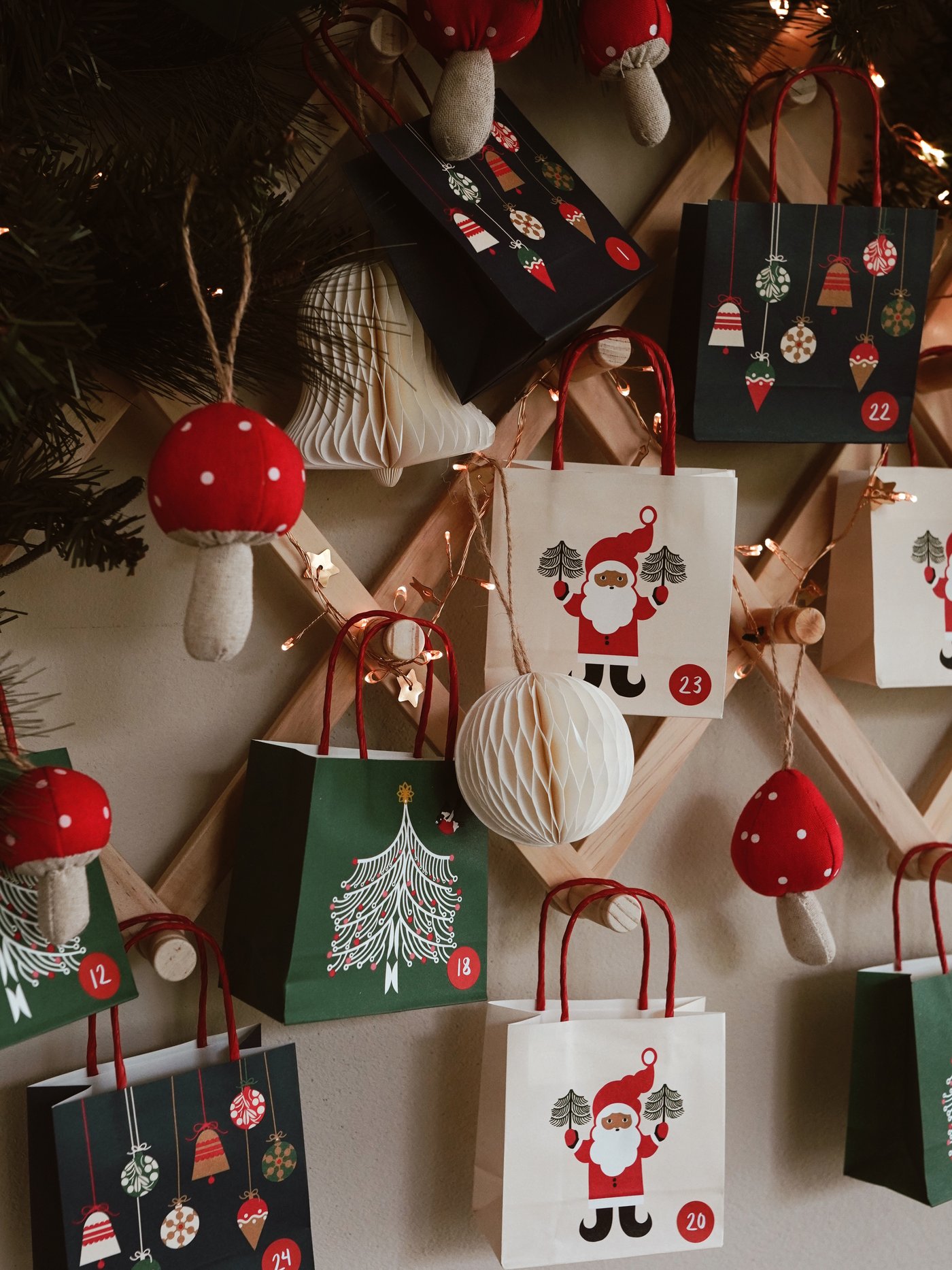 Weihnachts-Adventskalender mit kleinen Geschenktüten, die an einem Holzgitter hängen. Die Tüten sind mit Weihnachtsmannmotiven, Ornamenten und Zahlen verziert. Festliche und gemütliche Atmosphäre.