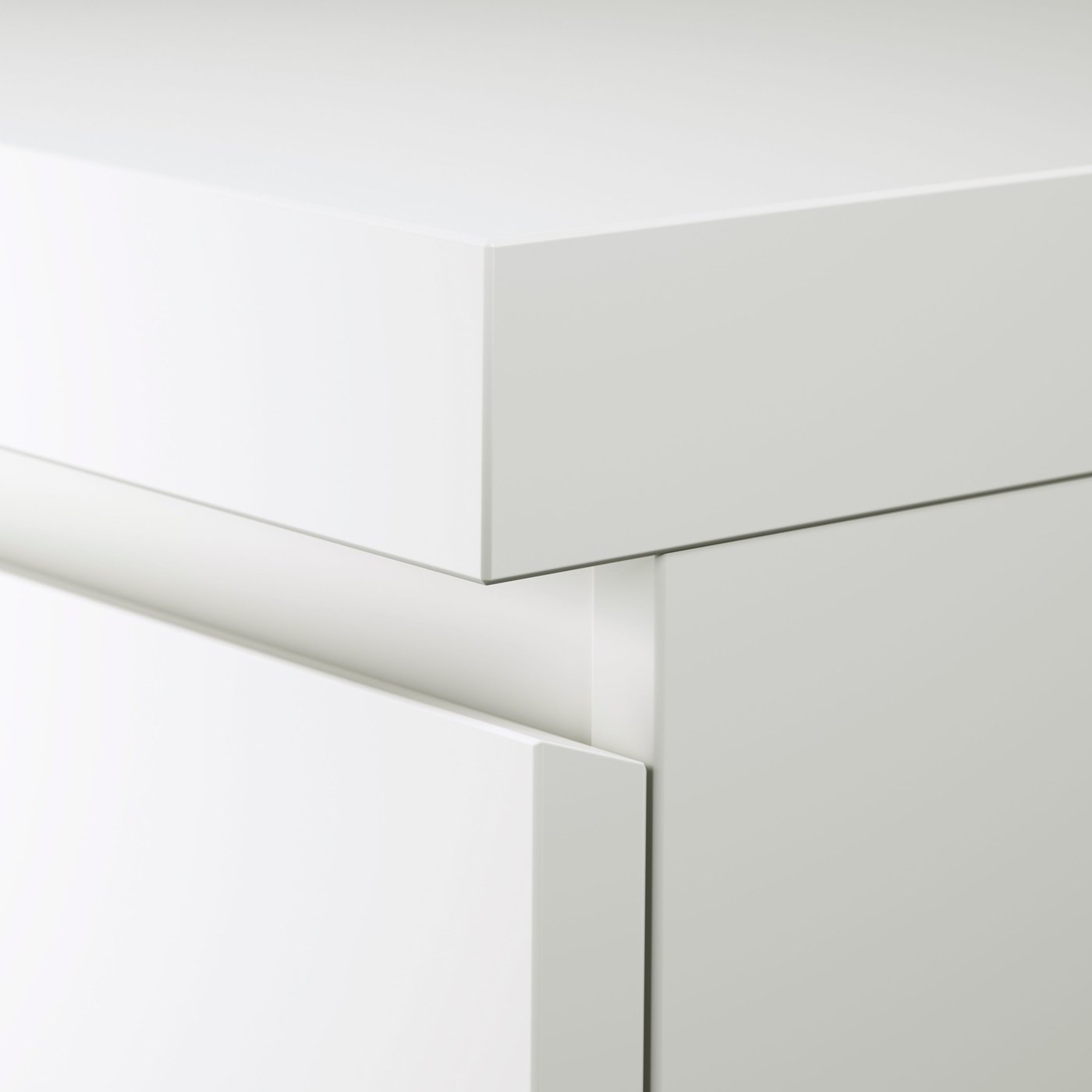 A corner of a white MALM desk showing some of the surface as well as the top part of the top drawer.