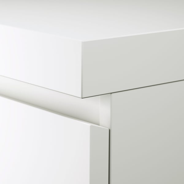 A corner of a white MALM desk showing some of the surface as well as the top part of the top drawer.