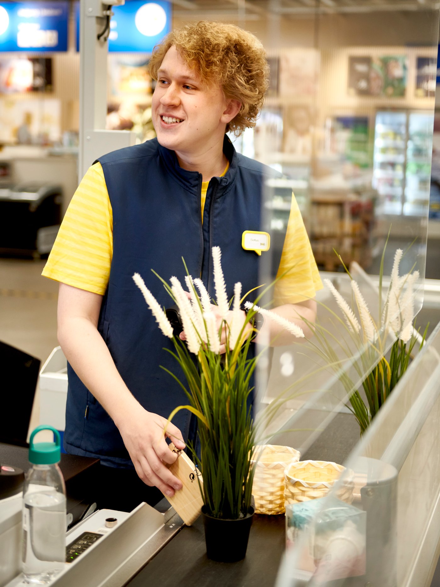Een IKEA medewerker plaatst een potplant op een kassa in een IKEA winkel.