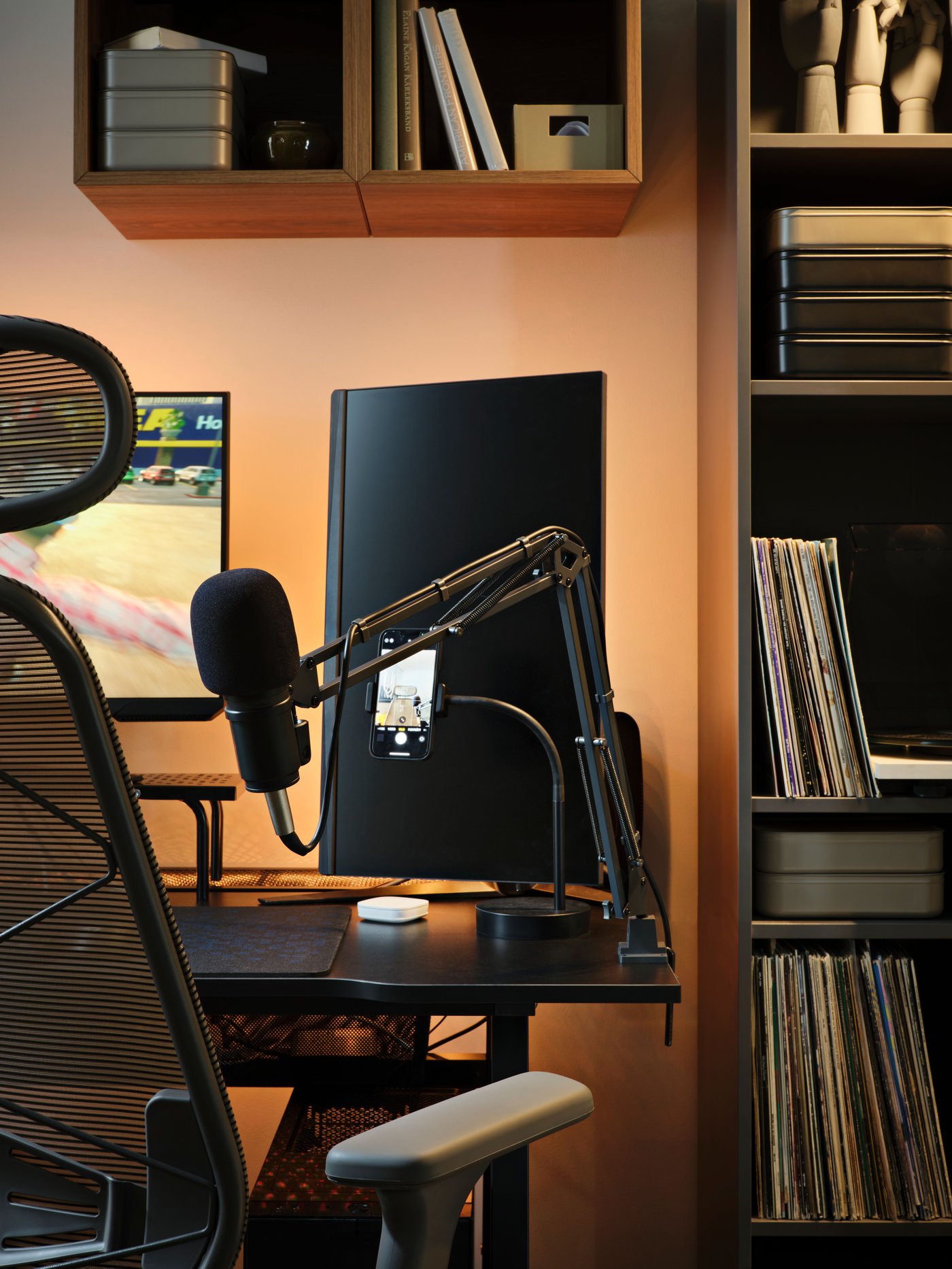 White light from an unseen ORMANÄS LED lighting strip shines through the metal mesh of a black gaming desk and monitor stand.