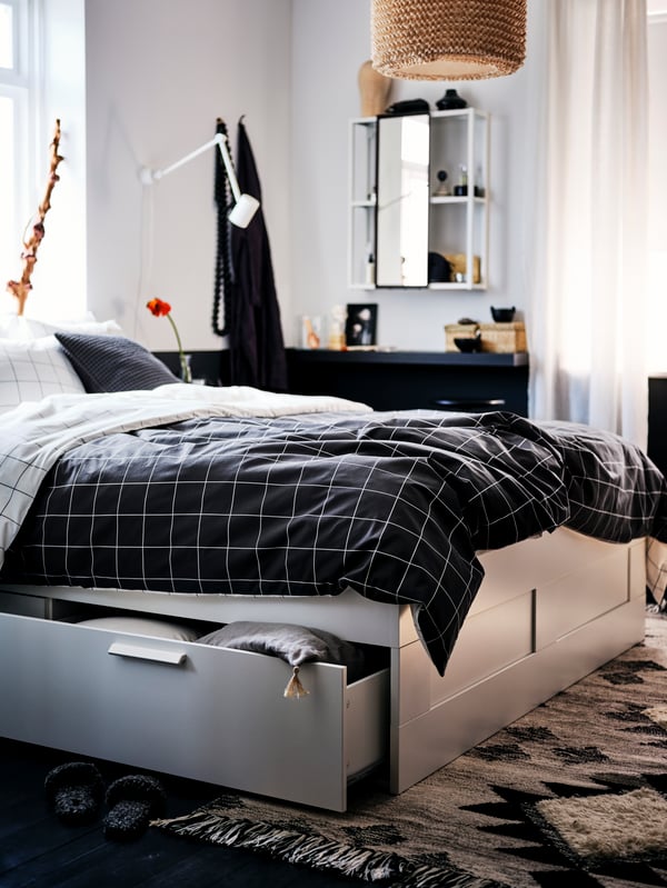 A bedroom with a white BRIMNES bed with storage made with black-and-white-chequered VITKLÖVER bed linen.