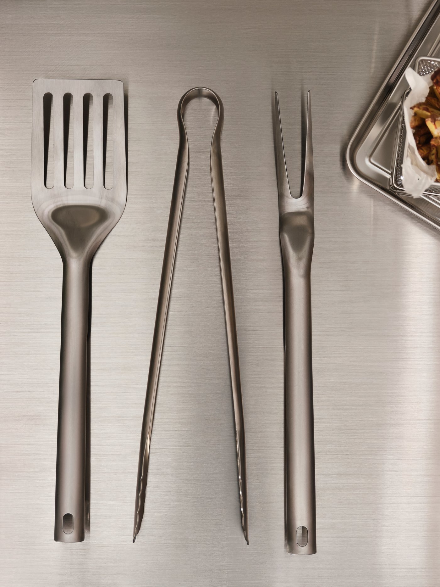 A GRILLTIDER three-piece, stainless-steel barbecue tools set laid out on a brushed-metal surface.