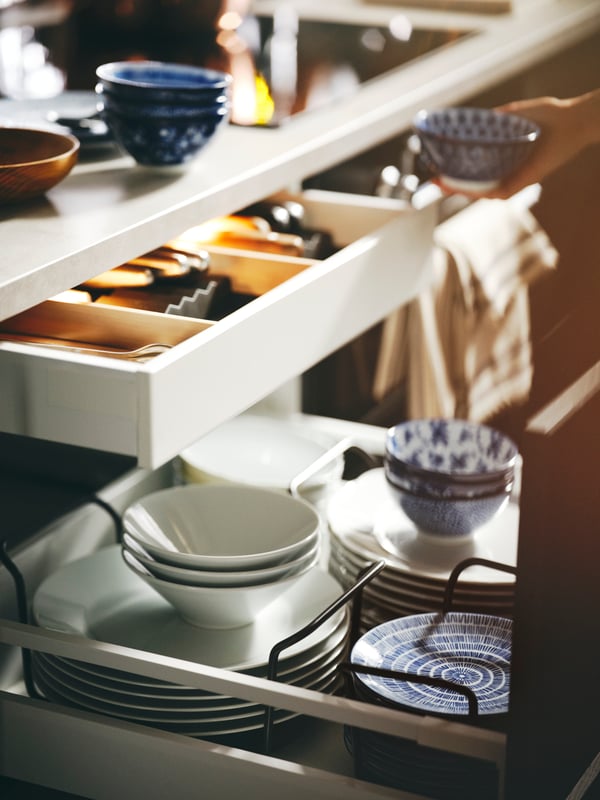 Dinnerware including patterned/blue ENTUSIASM bowls and side plates stacked in UPPDATERA plate holders inside an open drawer.