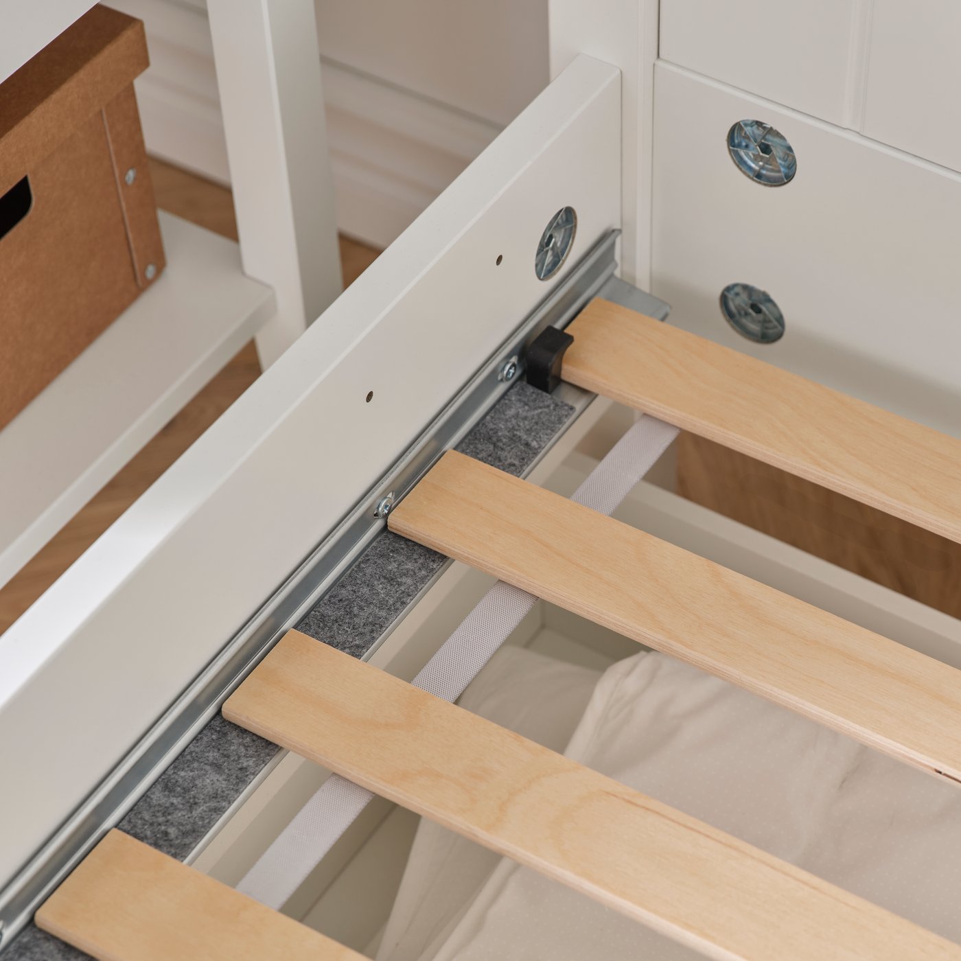 A close-up of a white GULLABERG bed frame with four storage boxes is shown, revealing a felt strip and slatted bed base.