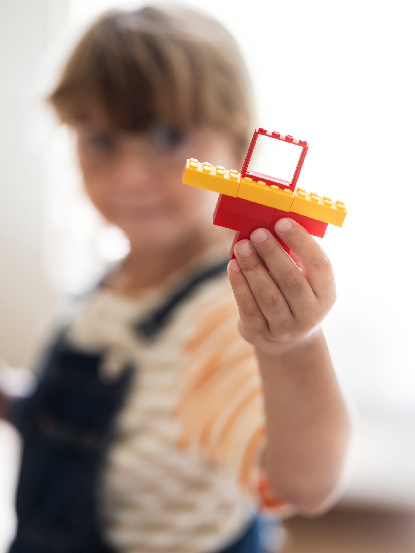 Enfant debout tenant une partie d’une maison en LEGO® à base d’éléments d’un ensemble BYGGLEK de 201 pièces.
