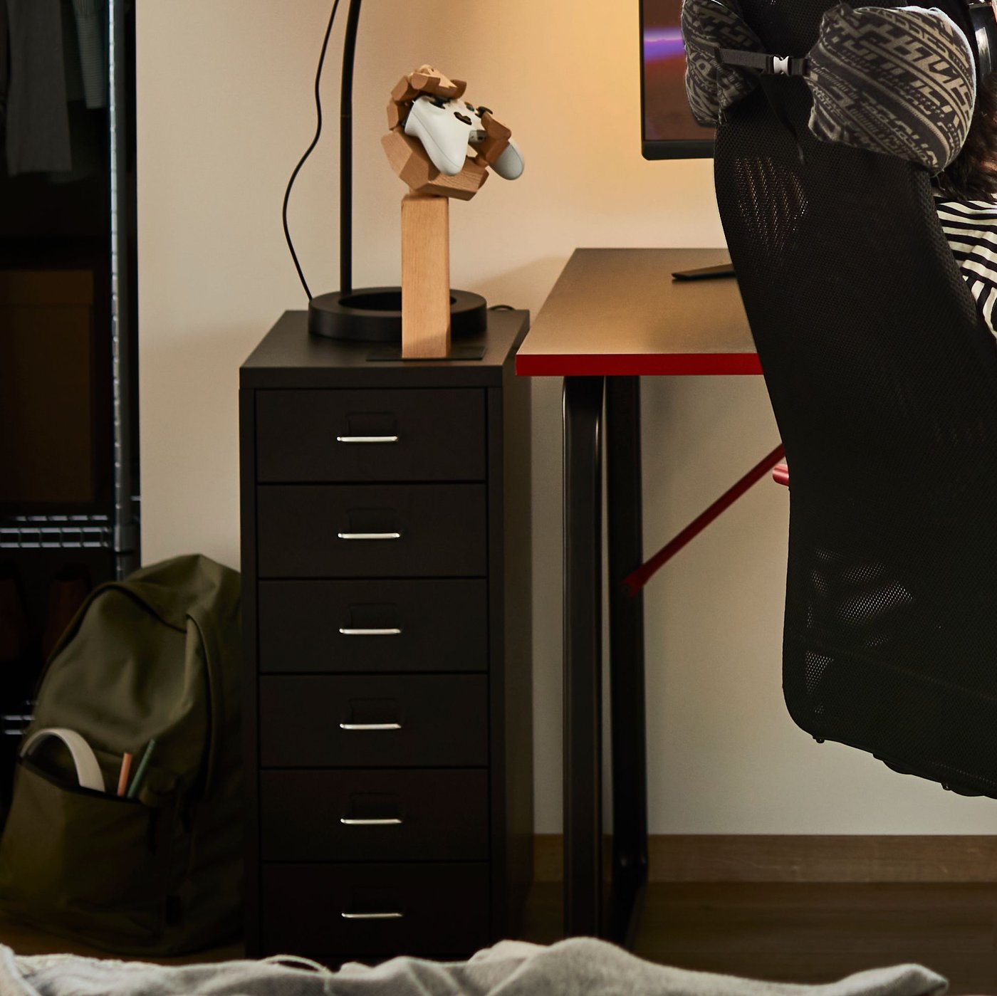 A black steel HELMER drawer unit on castors is by the side of a desk. A hand-shaped LÅNESPELARE accesories stand is on top.