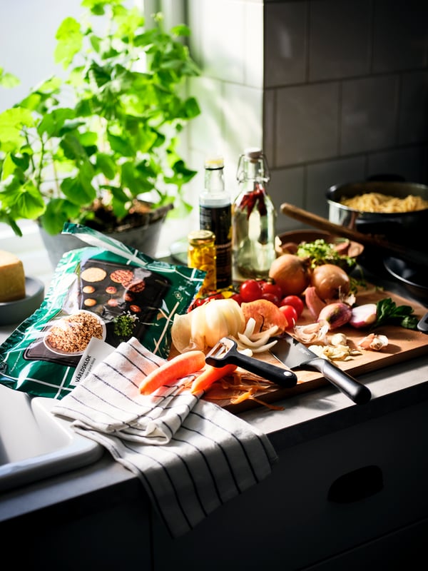 A worktop filled with ingredients in the middle of cooking prep, a RINNIG tea towel, and a bag of VÄRLDSKLOK plant mince.