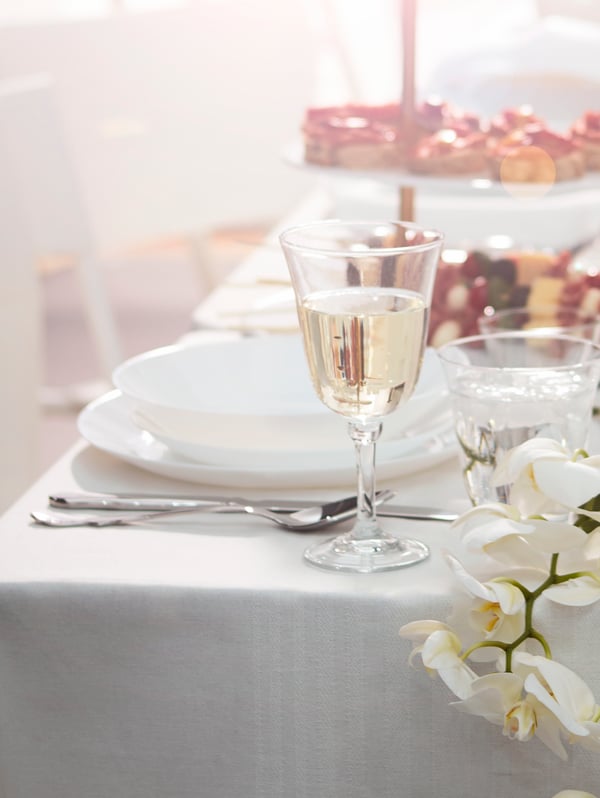 A large wedding table is set with white dinnerware and clear glassware