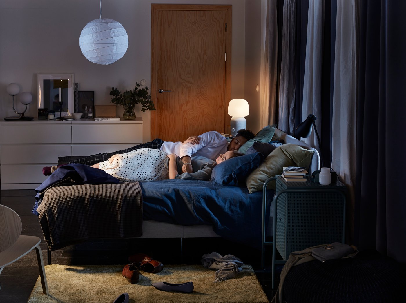 Un couple dort dans un lit rembourré SLATTUM ; on aperçoit en arrière-plan une lampe de table haut-parleur SYMFONISK allumée.