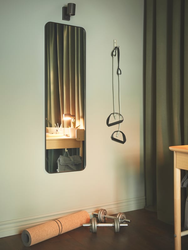Soba sa zelenom paletom boja i opremom za minimalističku teretanu koja je skupljena pored crnog LINDBYN ogledala ispod NYMÅNE lampe.