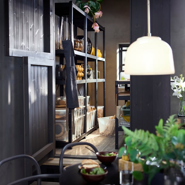 A shop storage with black BROR shelving unit displaying transparent boxes, vases and plants on its shelves.