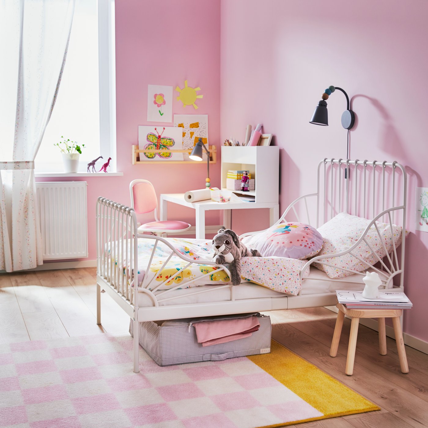 Habitación infantil color rosa con una cama extensible MINNEN blanca con respaldo en la cabeza y los pies. Al costado de la cama un escritorio infantil 