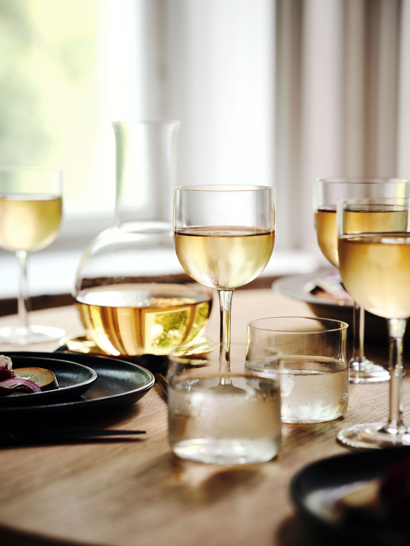 Près d’une fenêtre, une table garnie de verres à vin STOCKHOLM 2025 et d’autres verres, d’une carafe, d’assiettes et d’assiettes à salade.