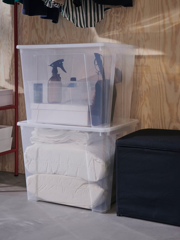 Two stacked SAMLA boxes with lids filled with household items below hanging clothes and beside a BOSNÄS footstool.