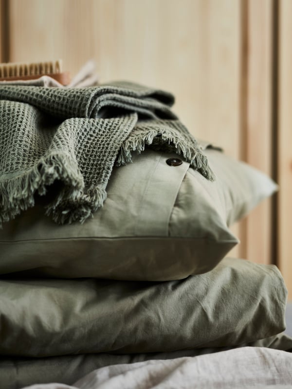 A folded light green VALLASÅN bath towel lies on top of a pillow and a duvet inside light green KRÅKRISMOTT bed linen.
