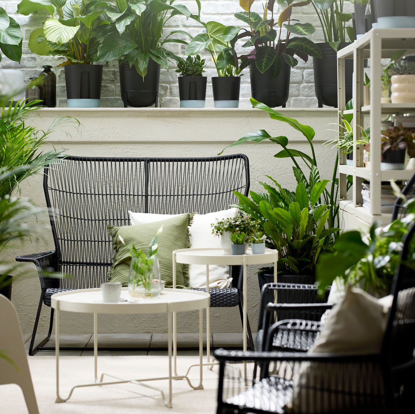 A sunroom with green plants and a TALLSKÄR outdoor 2-seat sofa with a KROKHOLMEN side table and coffee table in the middle.