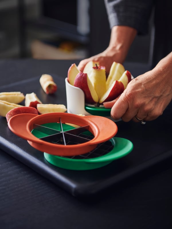 Some UPPFYLLD fruit cutters in a set of four in mixed colours, a person’s hands cutting an apple with the fruit cutter.
