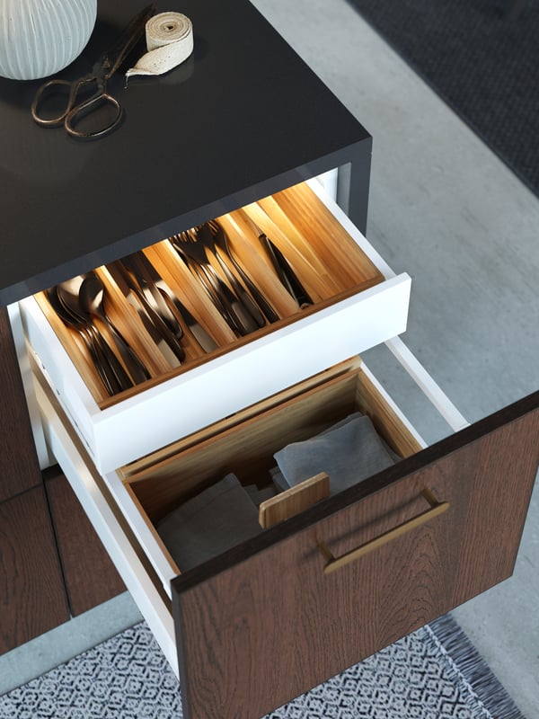 Open drawers on the kitchen island revealing neat wooden trays with cutlery and integrated lighting.