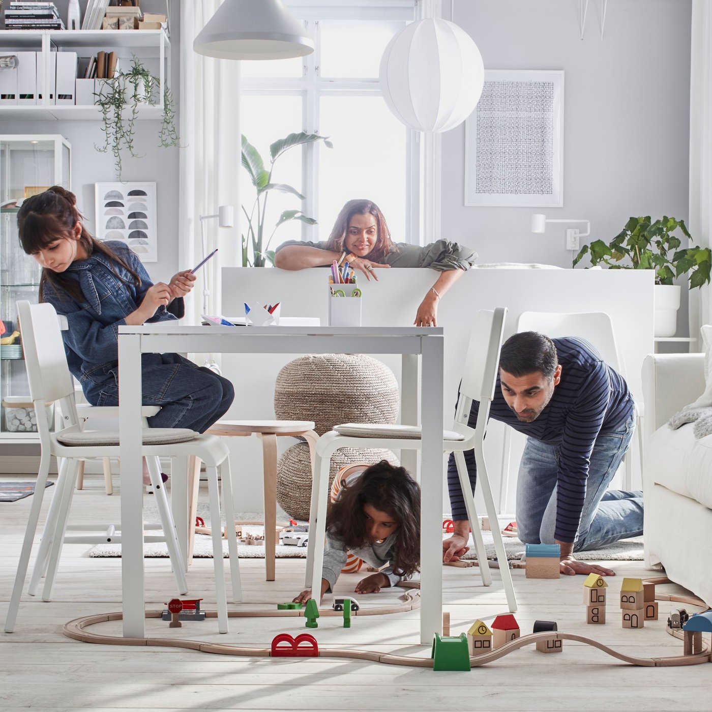 Salon blanc lumineux avec une famille de quatre personnes en train de jouer avec un set de train en bois LILLABO.
