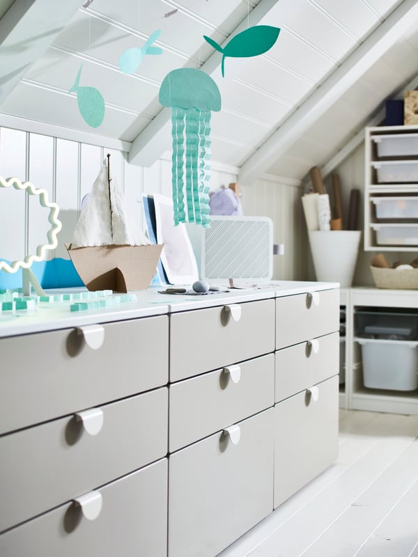 Three SMÅSTAD/PLATSA chests of 3 drawers stand in a row under some fish decorations hanging from a sloping ceiling.