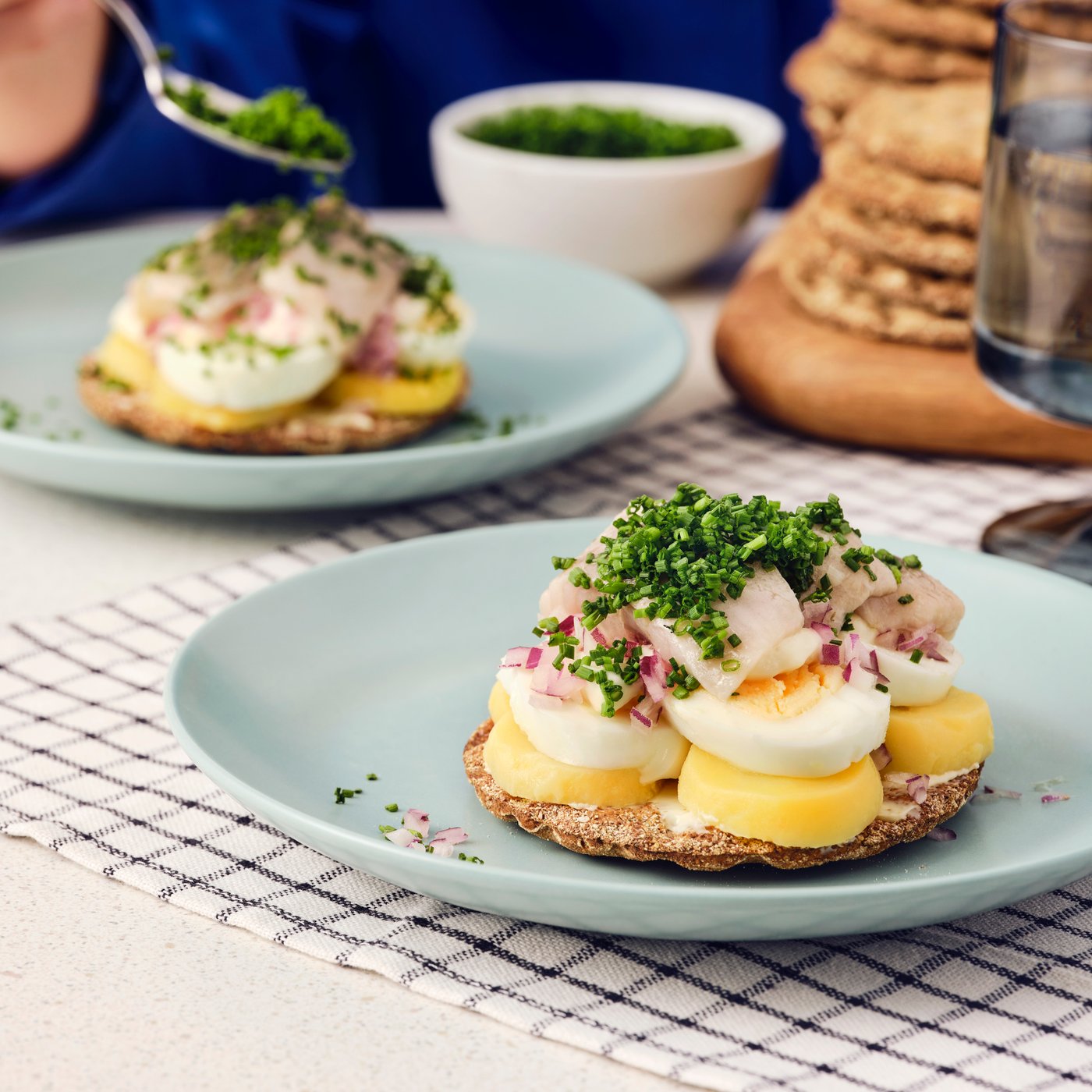Due panini realizzati con pane croccante di segale KNÄCKEBRÖD RÅG, uova, aringhe SILL DILL ed erba cipollina su piatti blu.