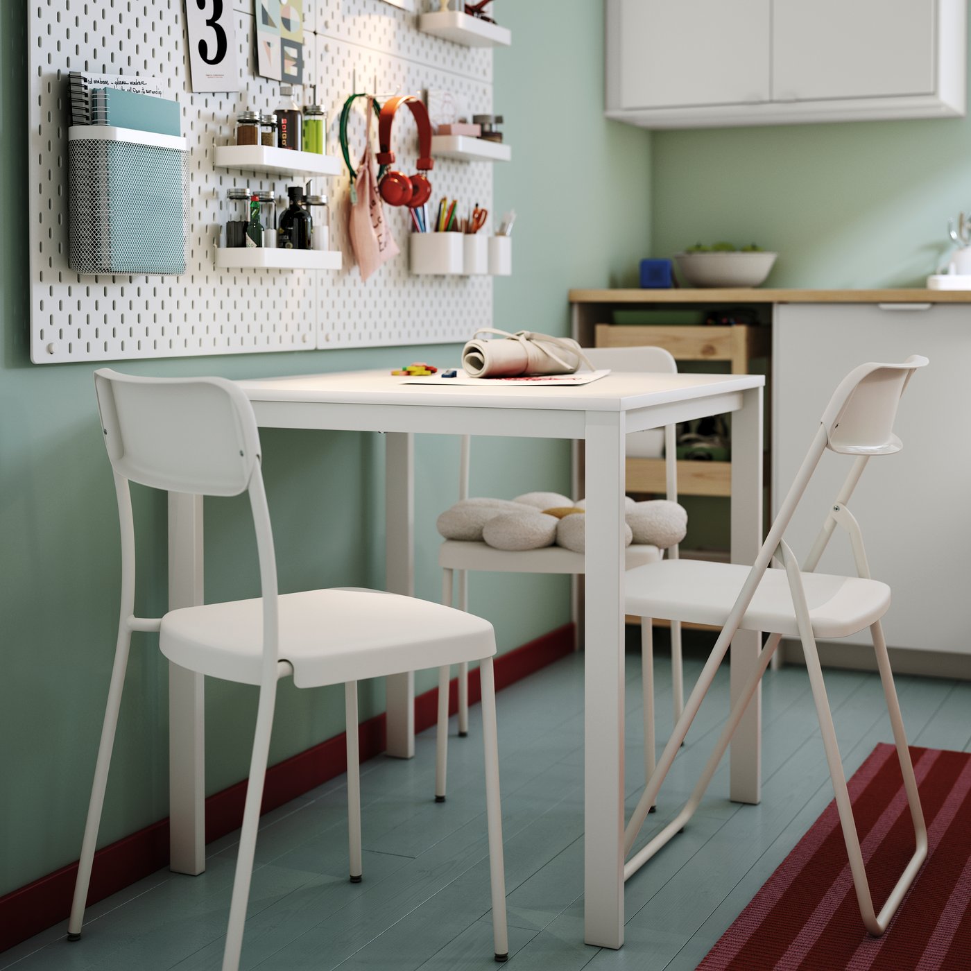 A white VIHALS table is set with green dishes, surrounded by a chair, with organised wall shelves in a light room.