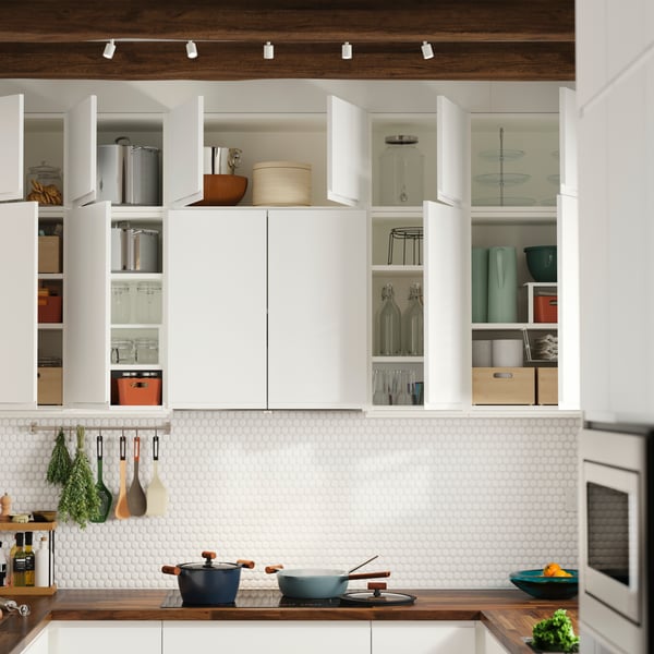 Les placards de cuisine muraux sont dotés de portes VOXTORP blanc mat ; certaines sont ouvertes, laissant apparaître les objets rangés à l'intérieur.
