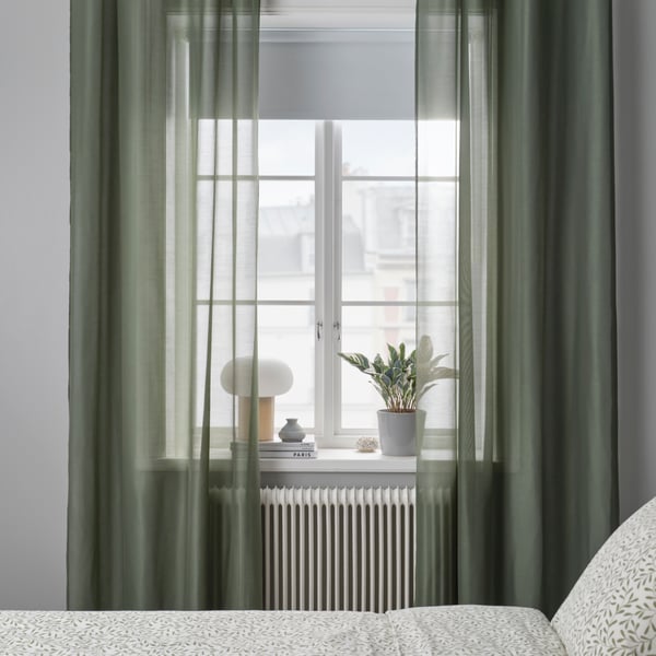 Fenêtre du salon avec de fins rideaux verts et une lampe de fenêtre. 