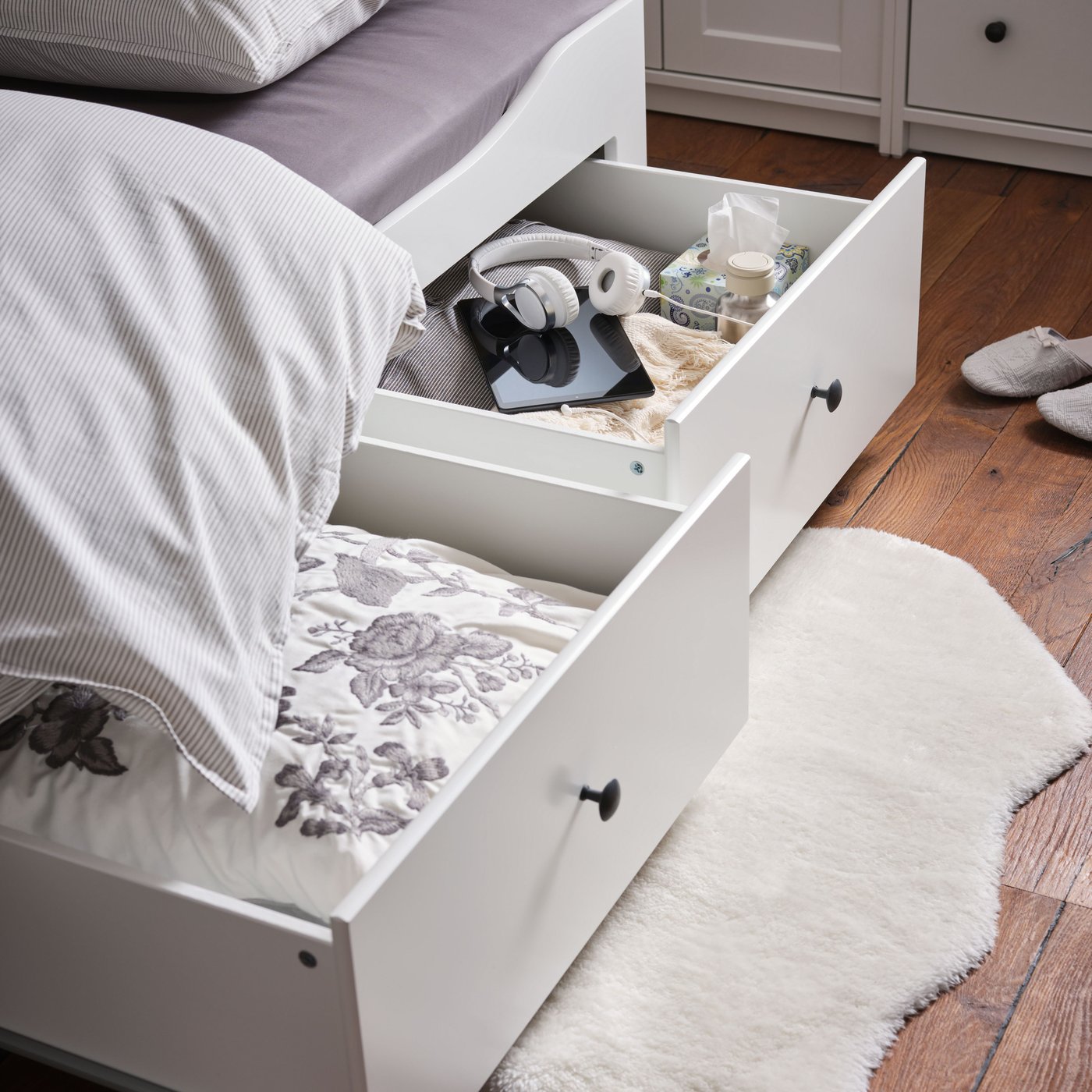 A white TOFTLUND rug lies on the floor underneath two open drawers of a HEMNES day-bed with 3 drawers/2 mattresses.